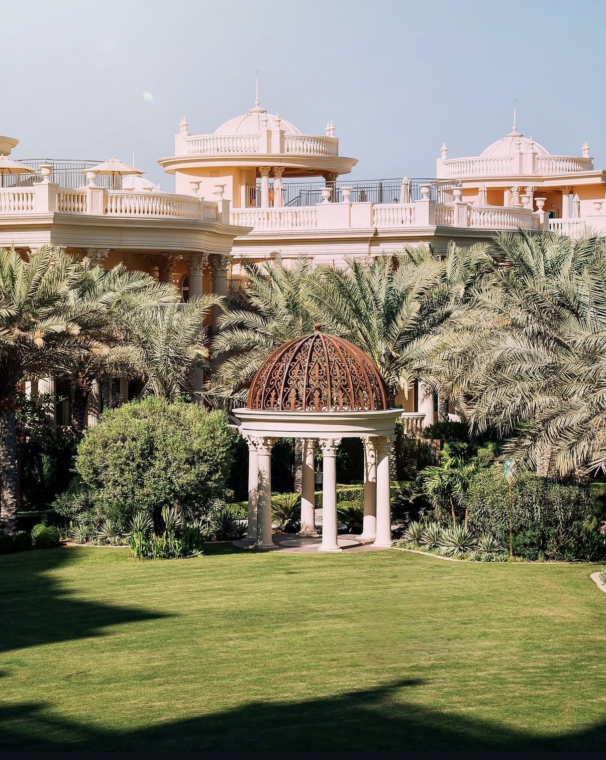 A white colonnaded gazebo with a copper filigree dome on a palace lawn among palms